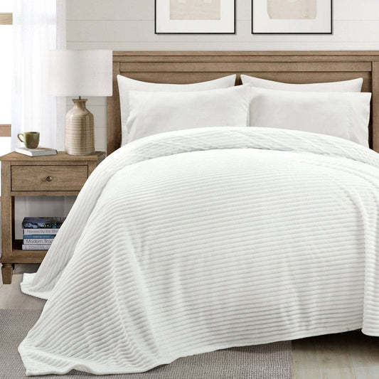 White quilted coverlet on a bed with pillows and a nightstand in a bedroom setting.faux fur blanket, oversized blanket, cozy bedding, luxury throw, bedroom decor