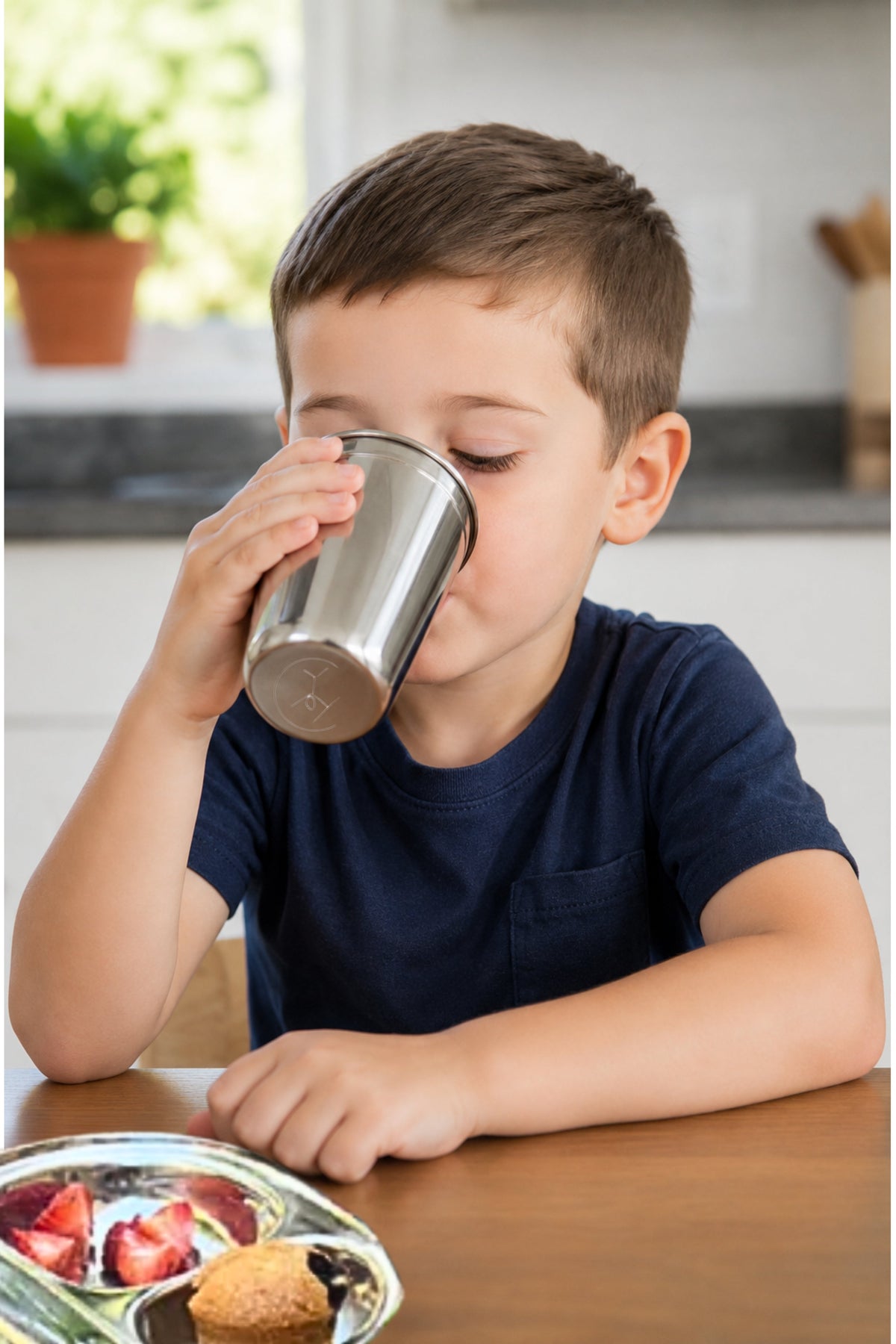 Child drinking from a metal cup at a table with a plate of food