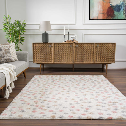 Living room with a wicker sideboard, gray sofa, and polka dot patterned rug with shades of cream, pink, white, beige. Powdery cream color blend.