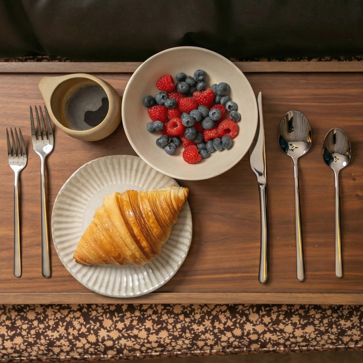 Breakfast setting with croissant, berries, and coffee on a wooden tray.