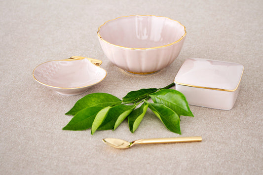 Set of ceramic bowls with gold accents on a textured surface with green leaves and a spoon.