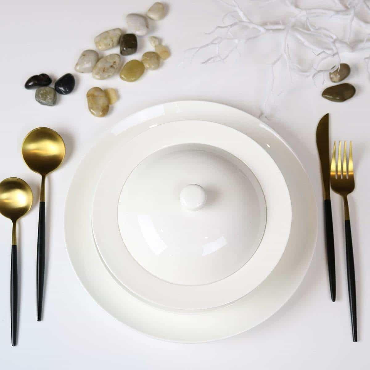 White ceramic bowls with gold and black cutlery on a white marble surface.