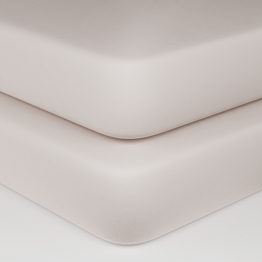 Close-up of two stacked mattress corners in a warm off-white or cream color, showing the textured fabric surface and rounded edges against a clean white background.