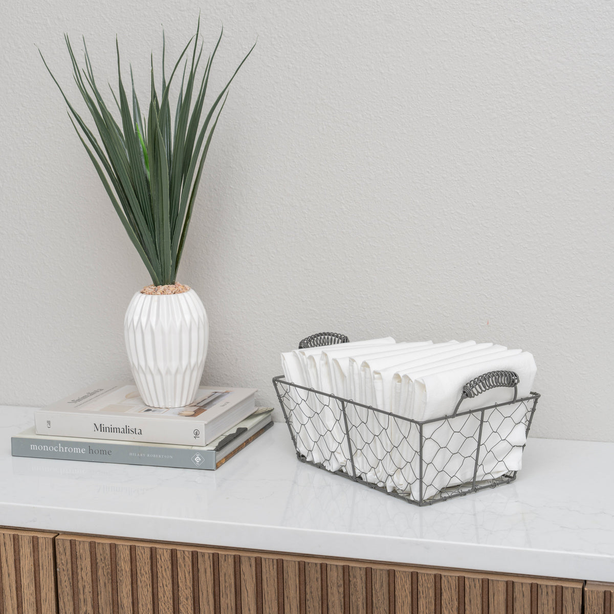 Decorative setup with a plant, books, and a wire basket on a surface.