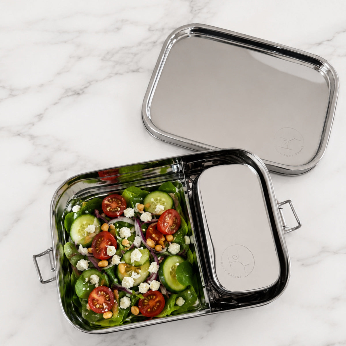 Stainless steel food container with a salad on a marble surface