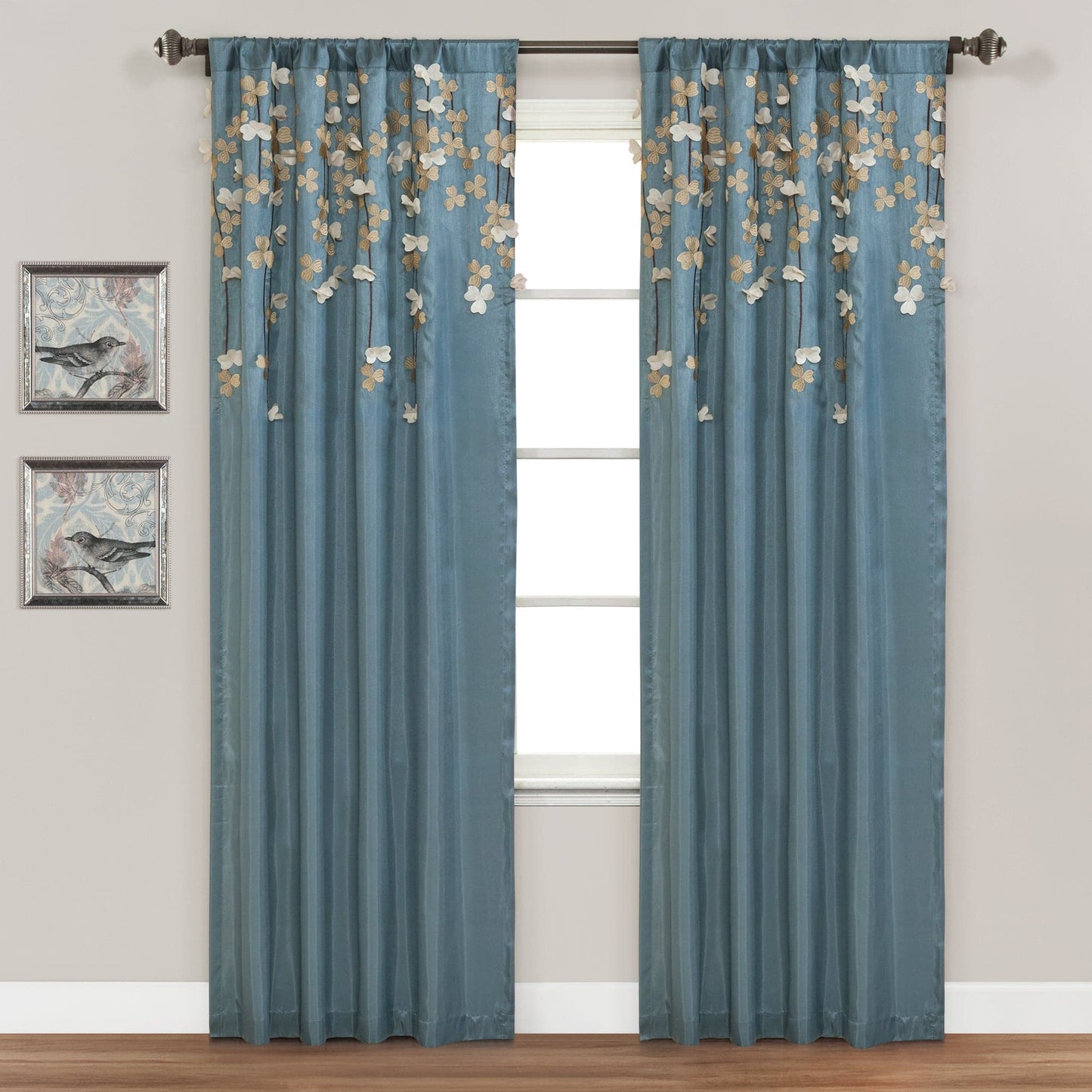 Blue floral curtains hanging in front of a window with wall art on the wall.