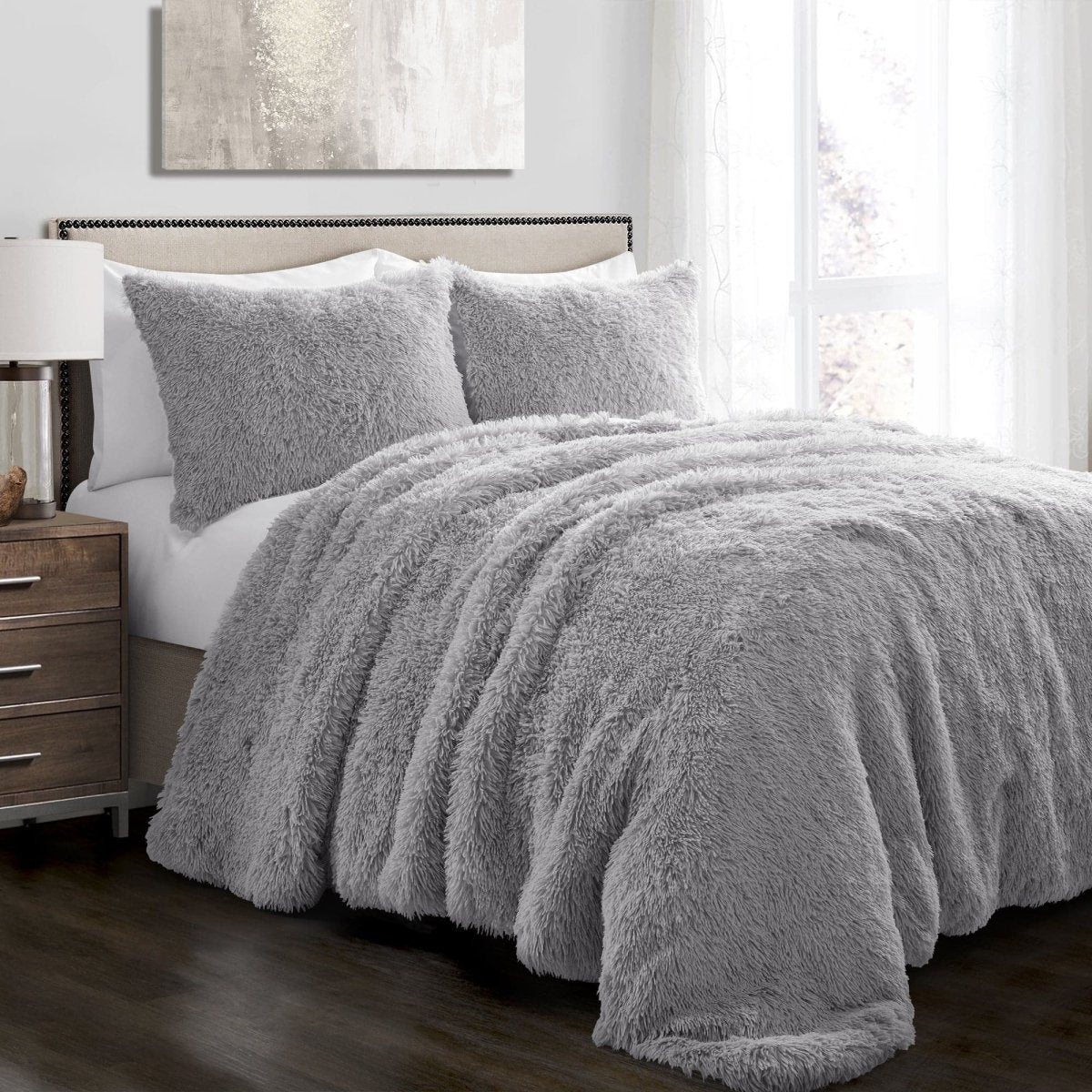 Gray fuzzy comforter on a bed in a bedroom setting with a nightstand and lamp.