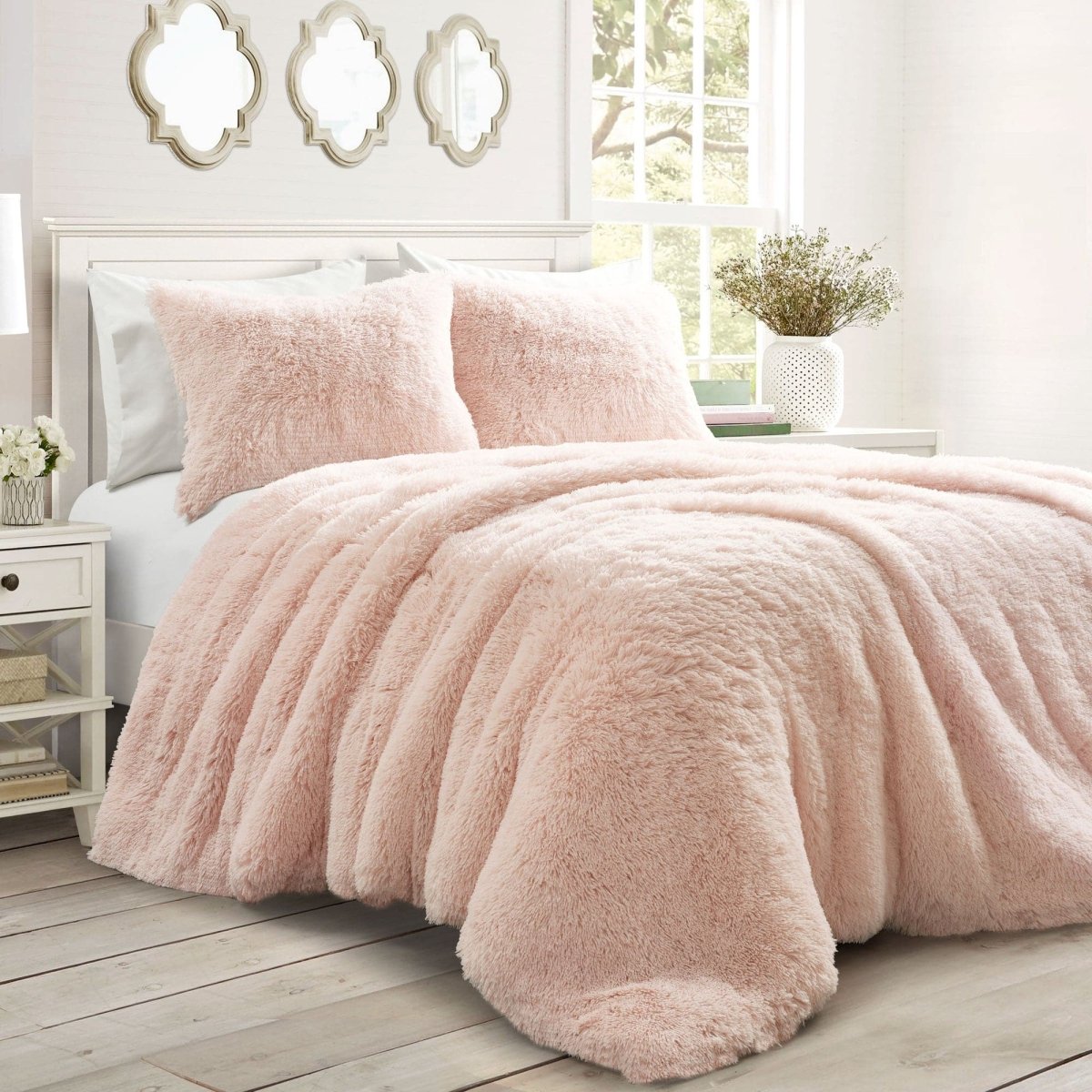 Pink fuzzy comforter on a bed in a bright bedroom with mirrors and a window. Faux fur bedding bed set.