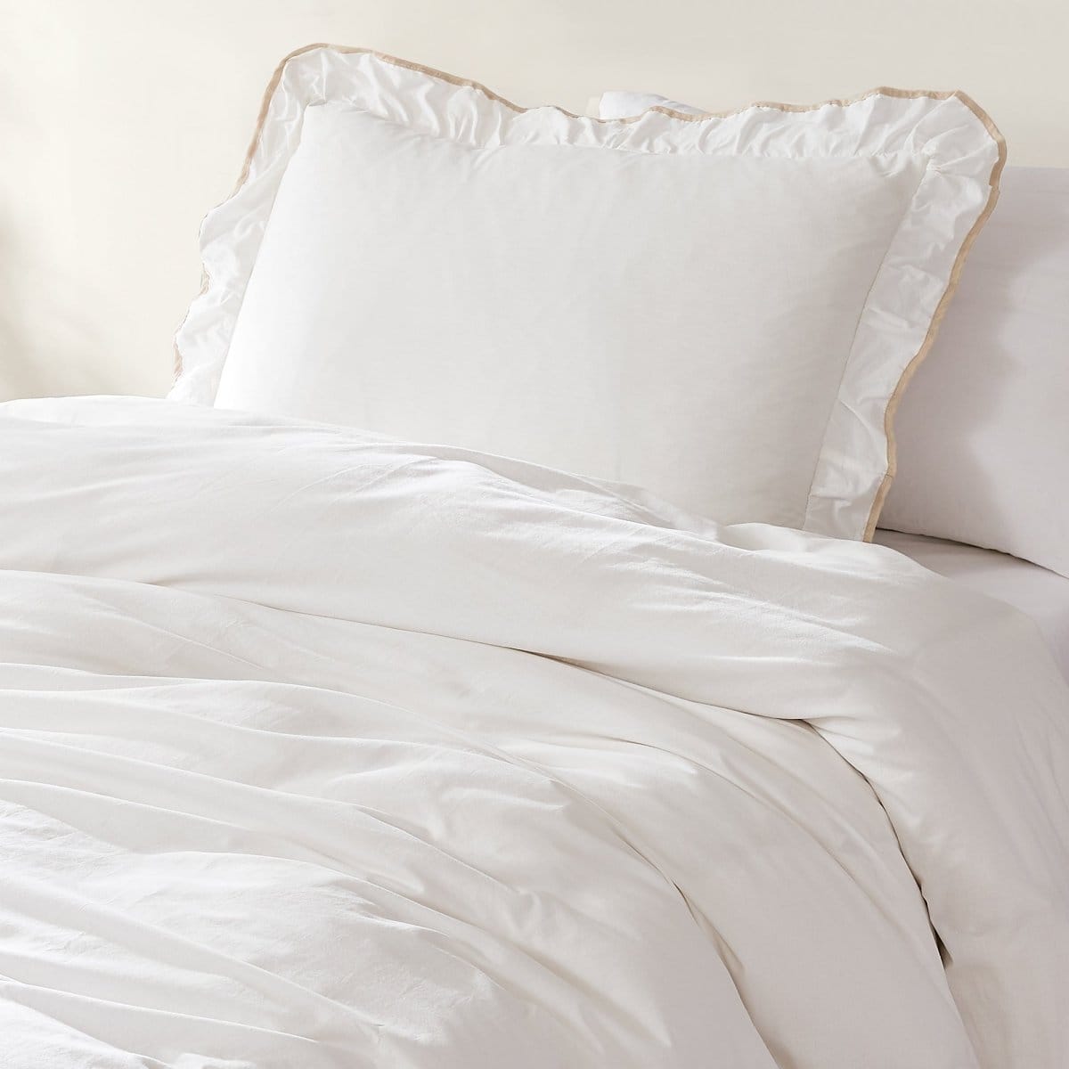 White bedding set with ruffled comforter and matching pillows on a bed. Duvet set.