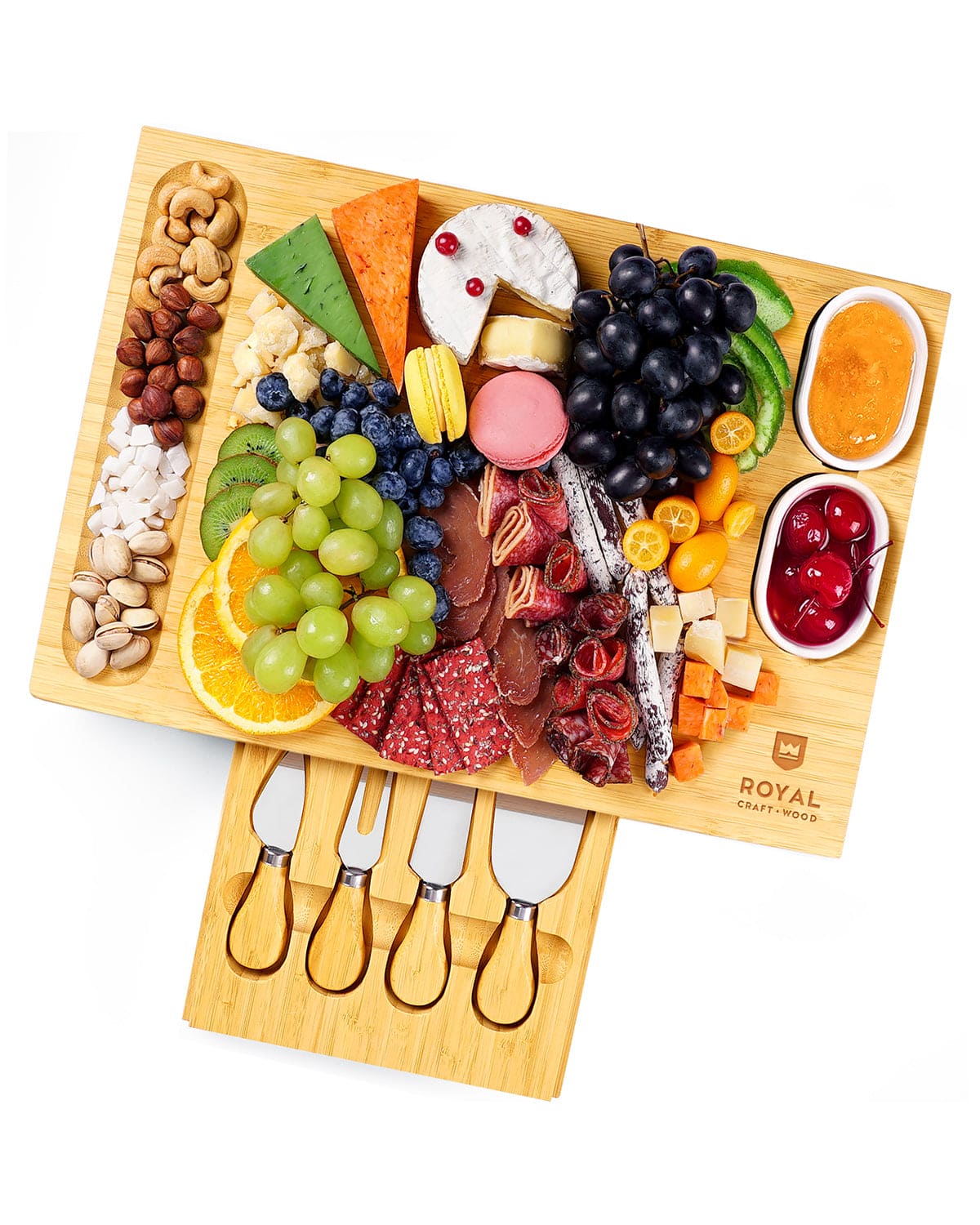 Wooden charcuterie board with assorted foods including fruits, meats, and cheeses, accompanied by four cheese knives.