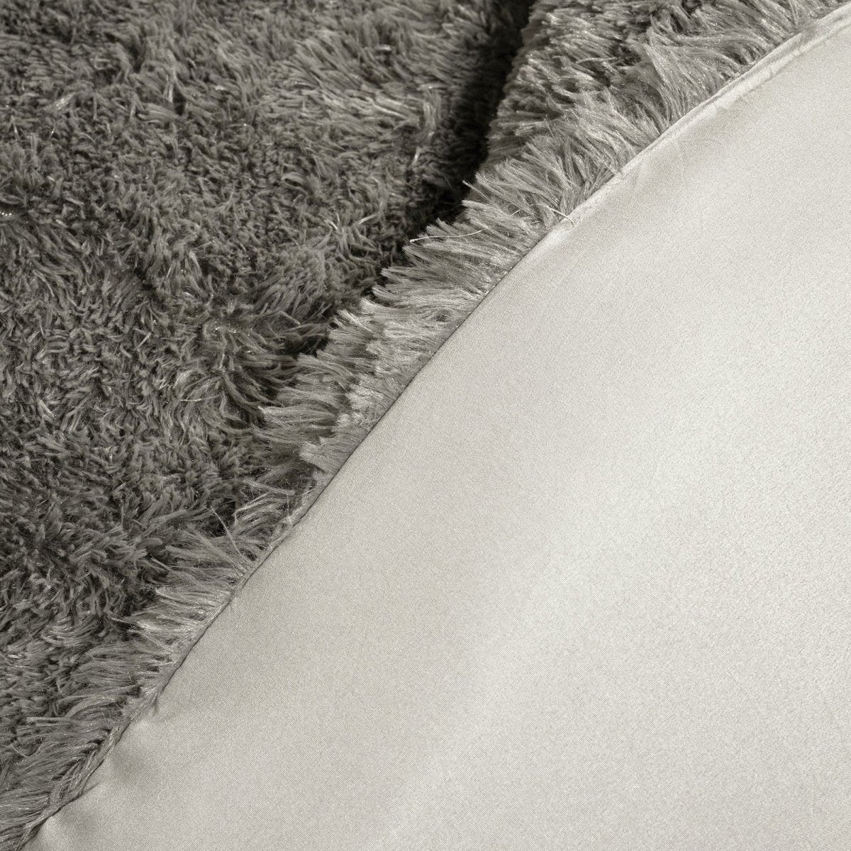 Close-up of a textured gray rug corner with a light-colored fabric surface. Faux fur bedding bed set.