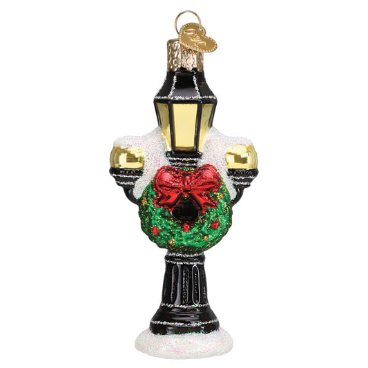 Bring a snowy street-scene detail to your tree with the Christmas Lamp Post Blown-Glass Ornament from Old World Christmas. A black lamp post with yellow lantern panels is decorated with a green wreath and red bow. White snow-style accents and glitter complete the wintry design, adding sparkle among your holiday ornaments.