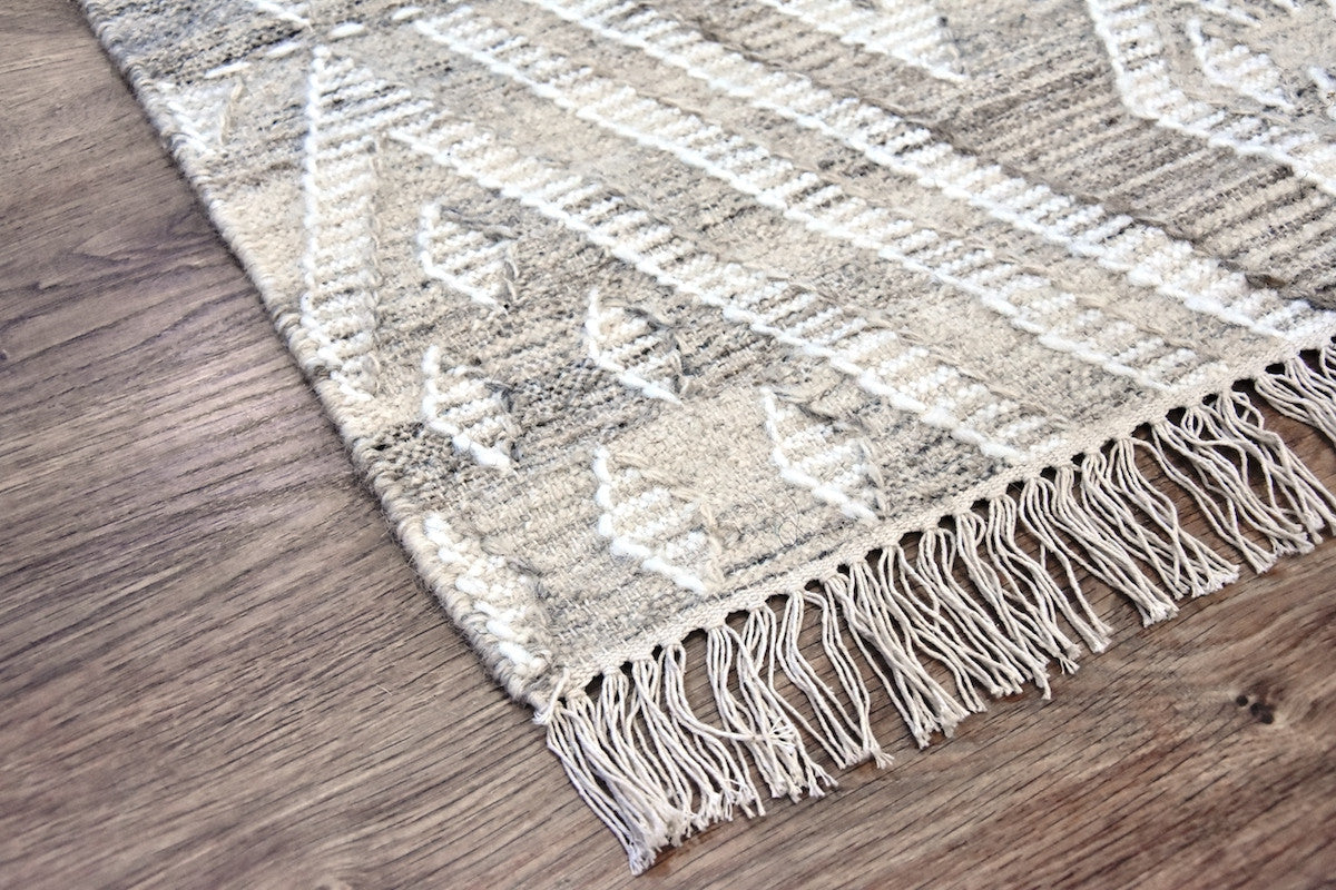 Textured area rug with geometric pattern and fringe on a wooden floor