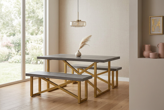 A modern dining set featuring a rectangular table and two matching benches with dark gray stone-look tops and gold-finished geometric metal bases, styled in a bright dining room next to a window. Mango wood