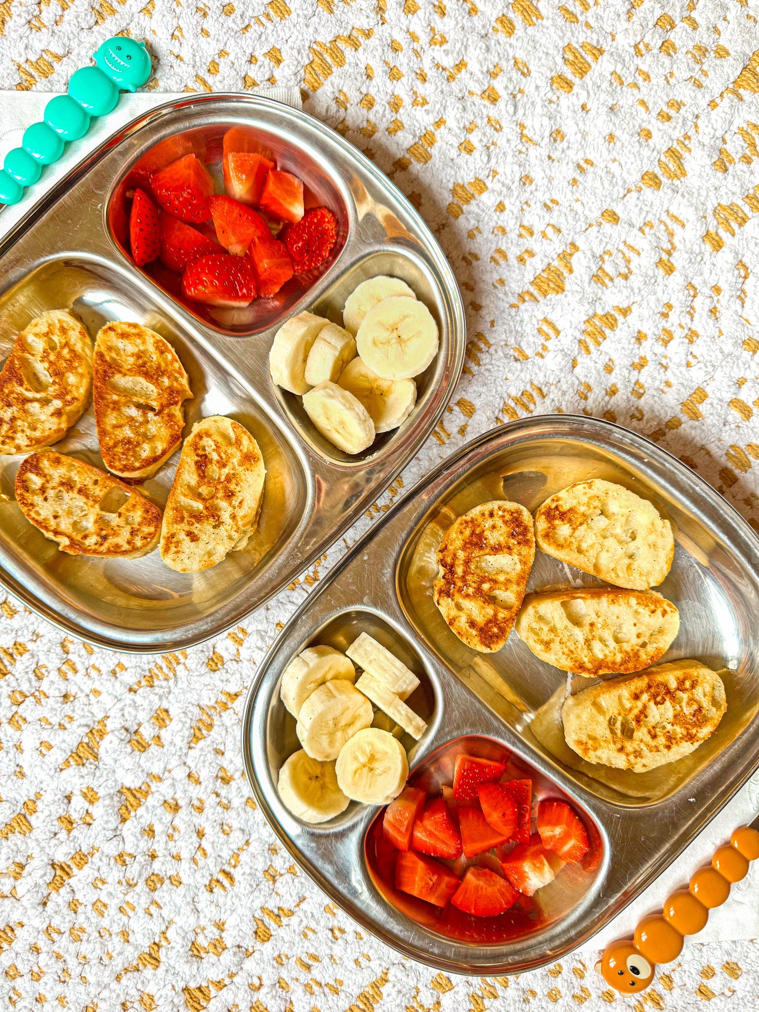 Two metal bento boxes with food on a textured surface