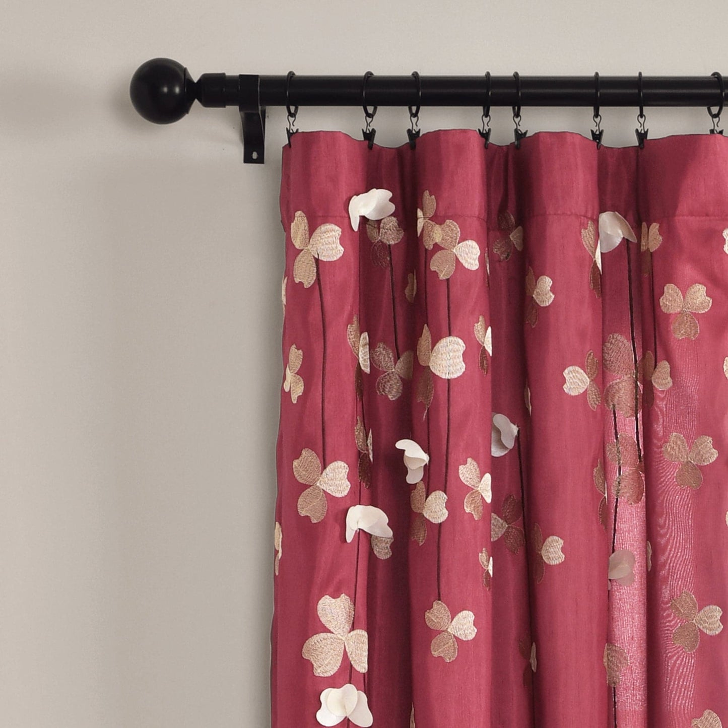 Red floral curtains with a black curtain rod on a beige wall