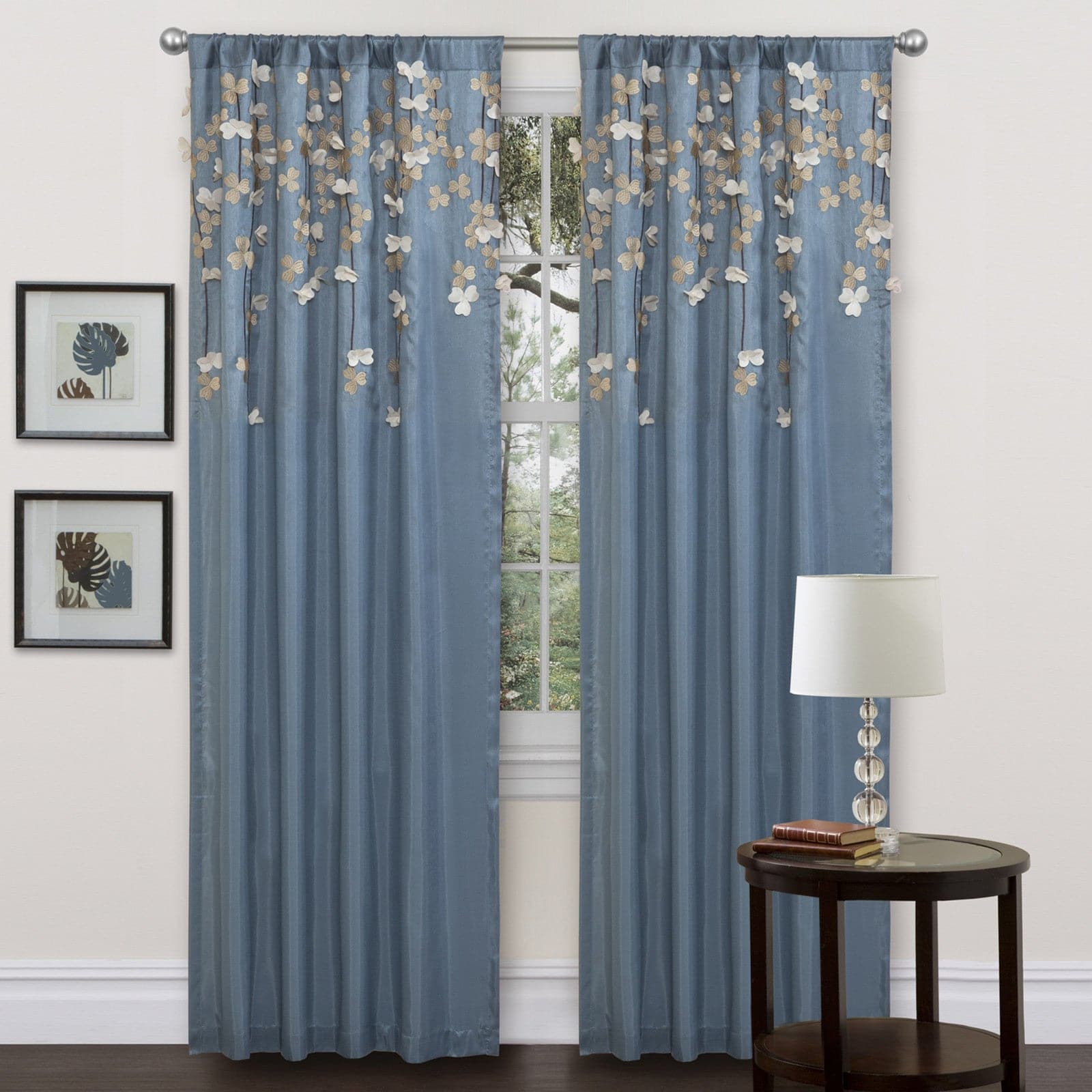Blue floral drop and embroidered flowers curtains with a side table and lamp in a room setting.