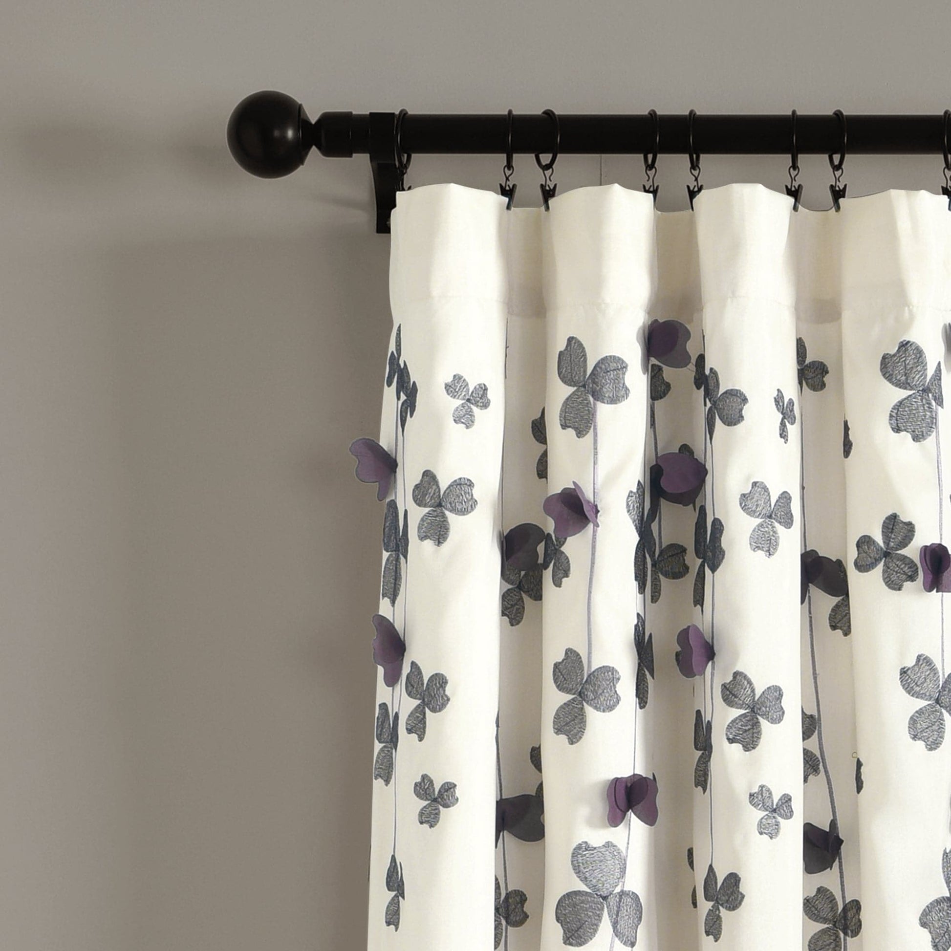 White curtains with purple floral patterns on a black rod against a gray wall.