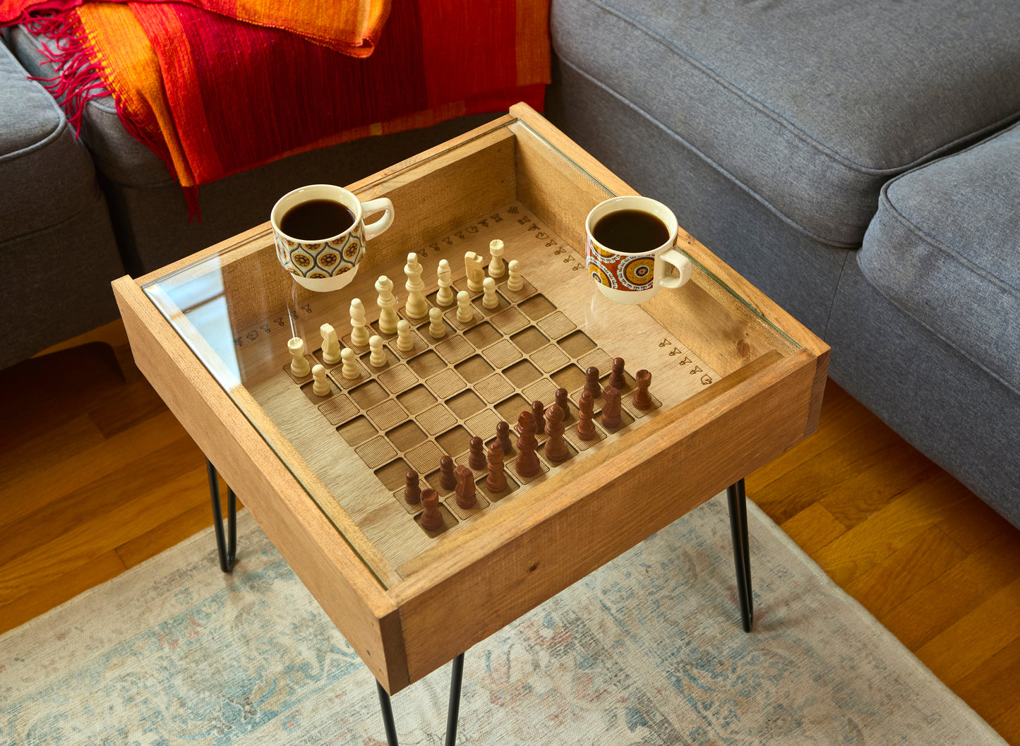 Wooden coffee table with chessboard and pieces, two cups of coffee on a living room floor.