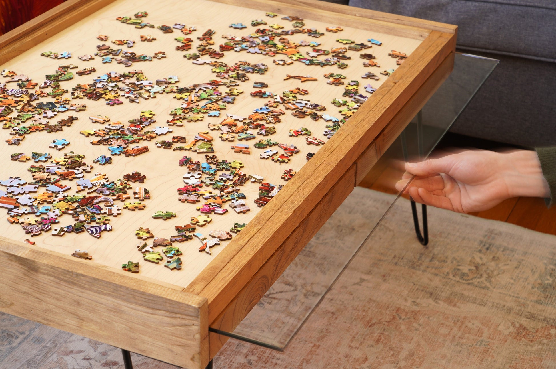 Puzzle table with a partially completed puzzle and a hand reaching for a piece.