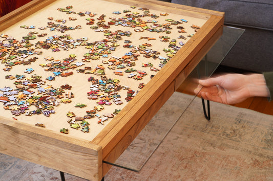 Puzzle table with a partially completed puzzle and a hand reaching for a piece.