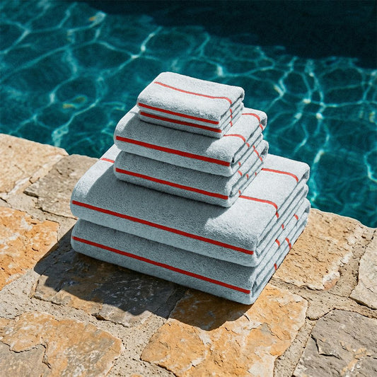 Stack of gray towels with red stripes on a stone ledge by a pool.