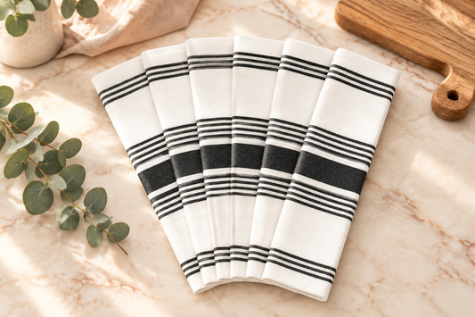 Six white knit napkins with black horizontal stripes, fanned out against a solid white background.