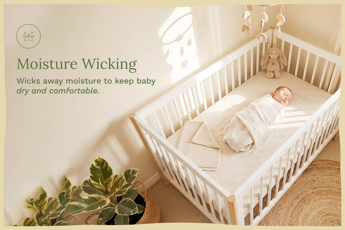 A baby sleep sack and blanket are shown inside a white wooden crib with a sleeping baby swaddled in them. The scene is styled in a warm, sunlit nursery with a plant, woven rug, and text overlay that reads 'Moisture Wicking' and 'Wicks away moisture to keep baby dry and comfortable.