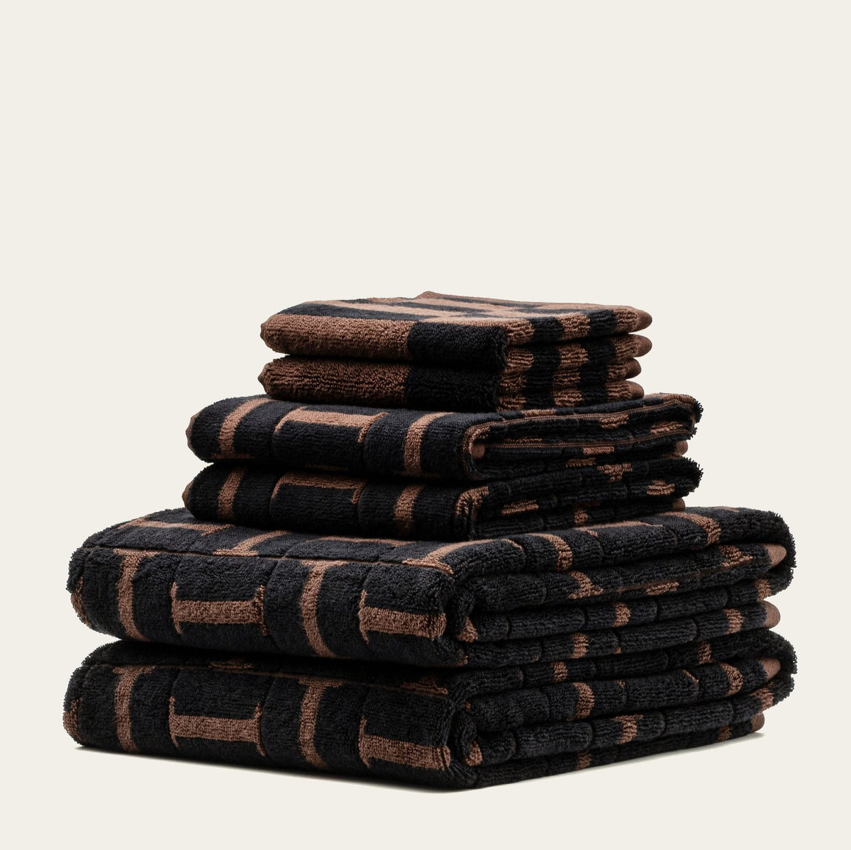 A stack of folded bath towels in a dark brown and black striped pattern, set against a solid off-white background.