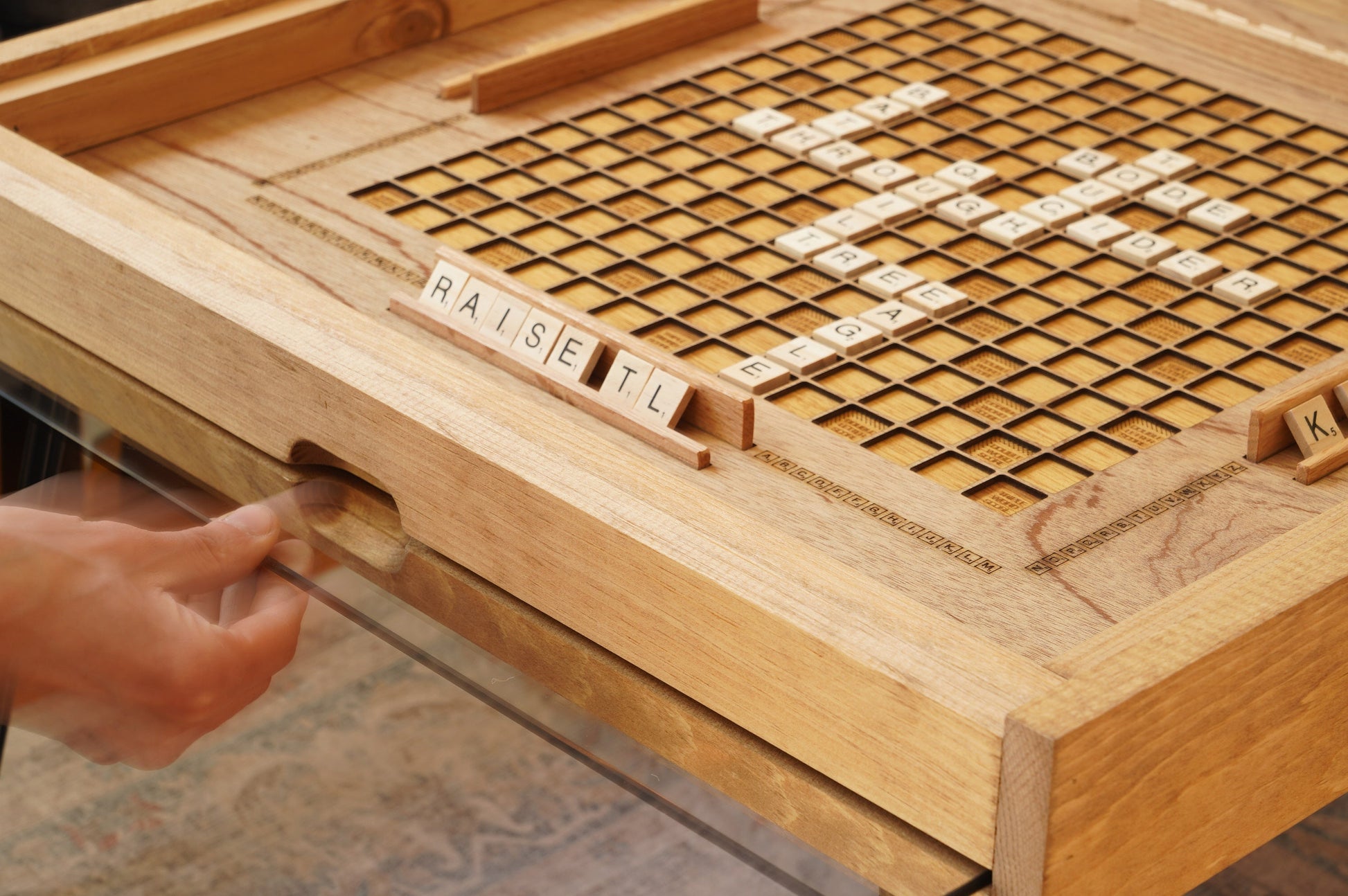 Wooden scrabble board with tiles and a hand reaching for a tile.