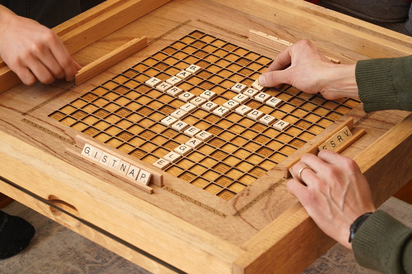 Two people playing scrabble a board game with wooden tiles on a wooden table.