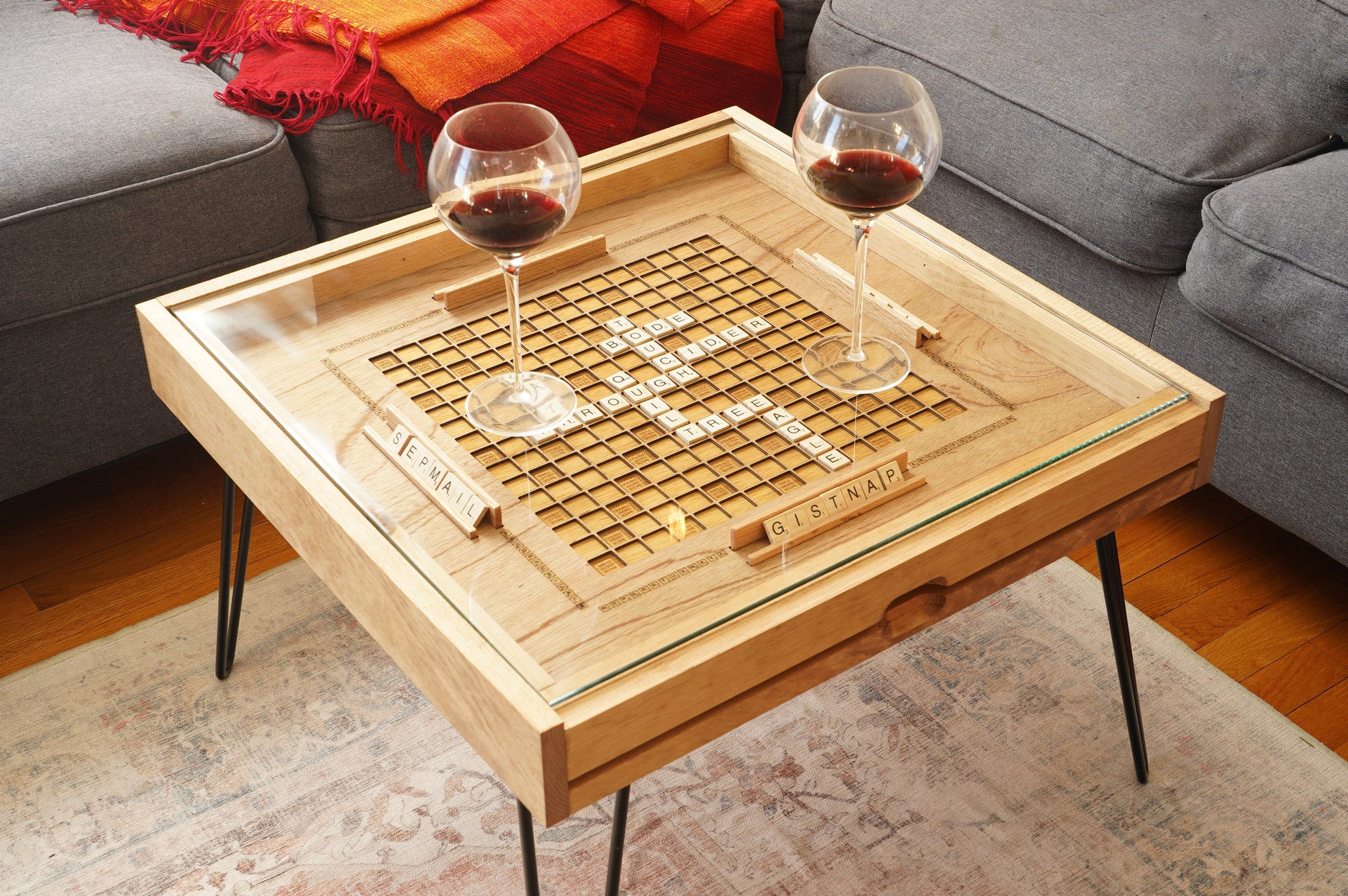 Wooden coffee table with a scrabble board and two glasses of red wine in a living room setting.