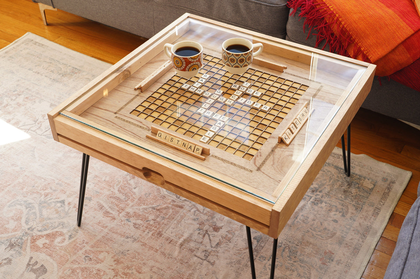 Wooden game table with a chessboard design, two cups of coffee, and a remote control on a rug.