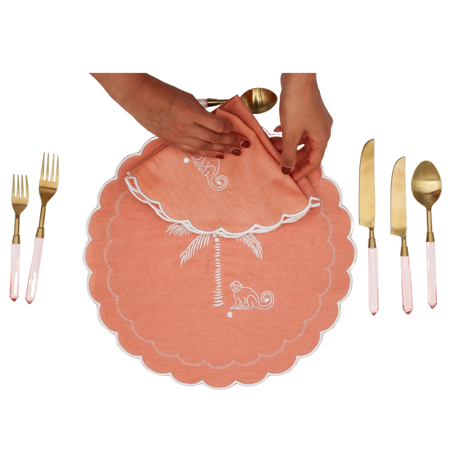 Coral placemat with white design, gold and pink cutlery on a white background