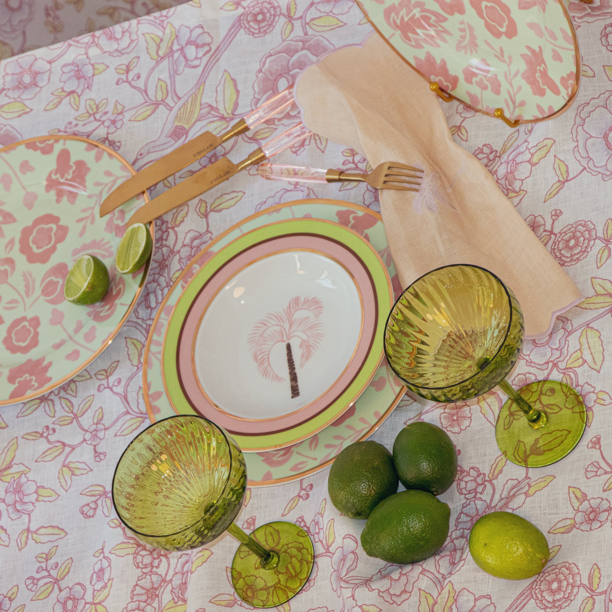 Table setting with floral tablecloth, plates, glasses, and limes on a decorative surface.24pc Peony Blush cutlery set with gold finish and rose petal handles by Ro'Table