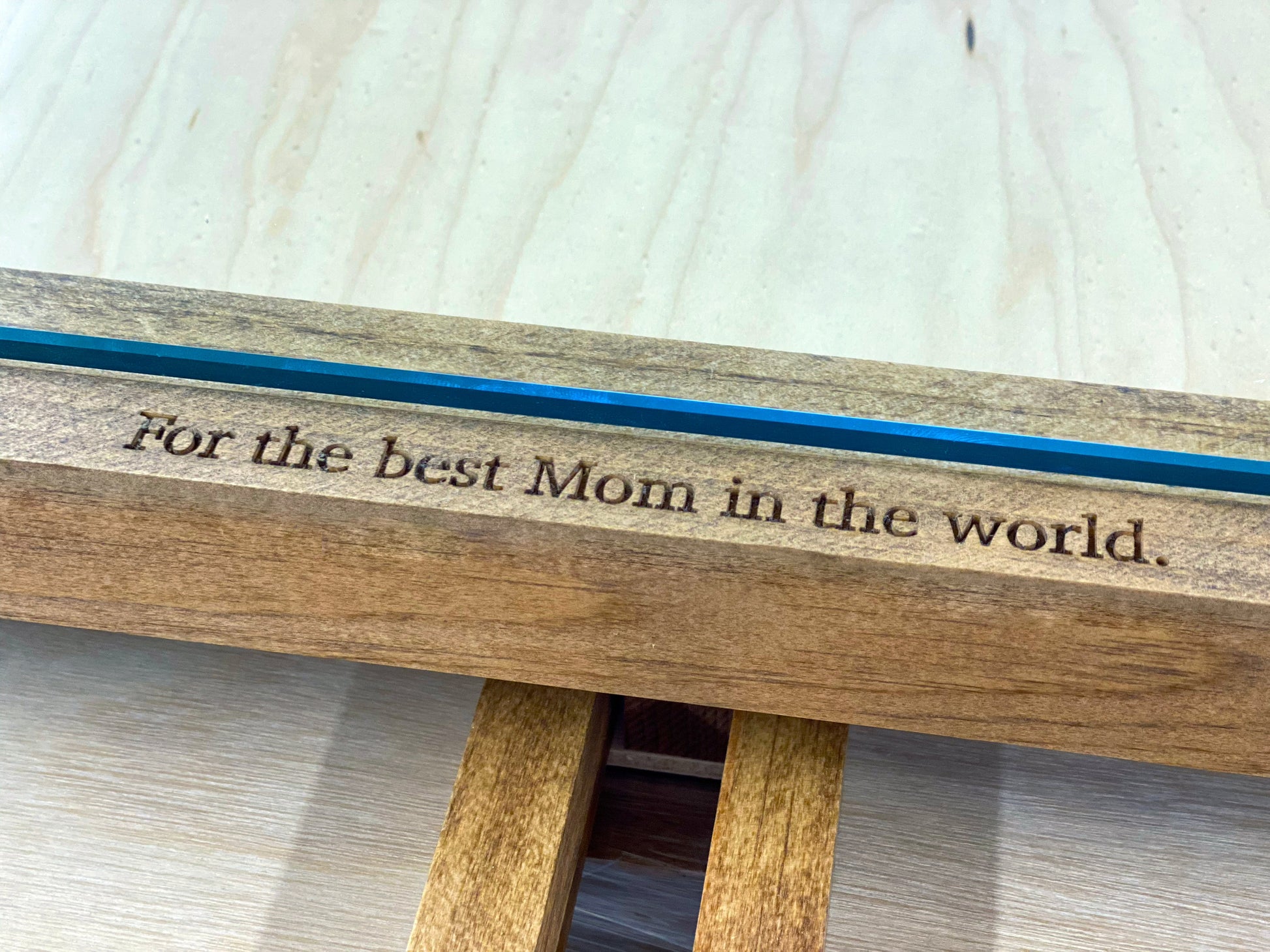 Wooden bench with engraved message 'For the best Mom in the world' on a light wooden floor.