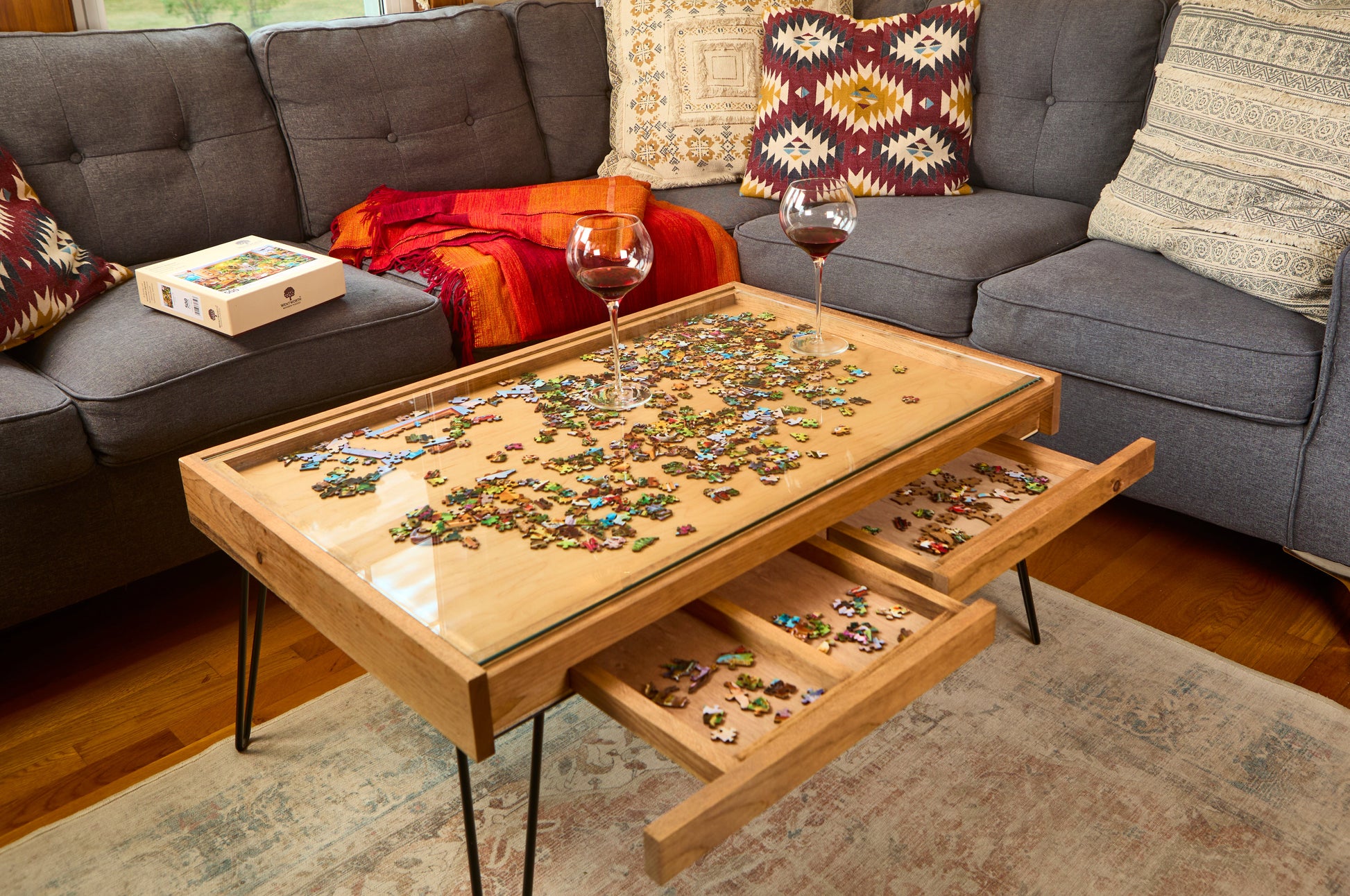 Wooden coffee table with puzzle pieces and drawers, placed on a gray sofa.
