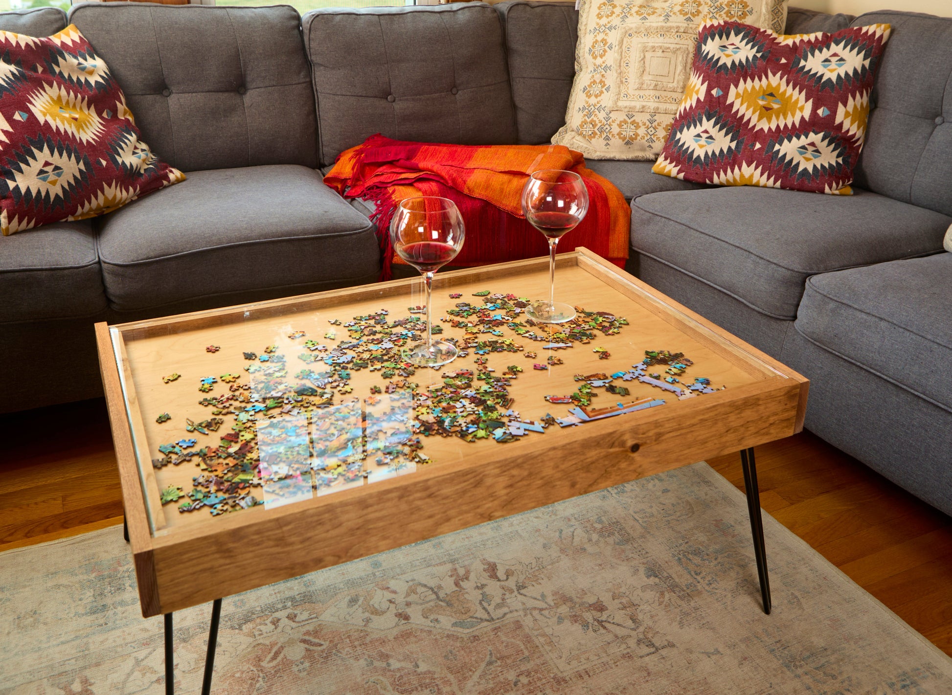 Wooden coffee table with a puzzle on top in front of a gray sofa with patterned cushions.