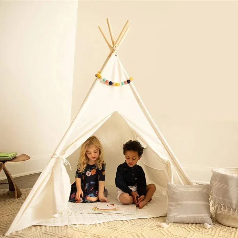 Two children sitting inside a white teepee in a room with a neutral color scheme.