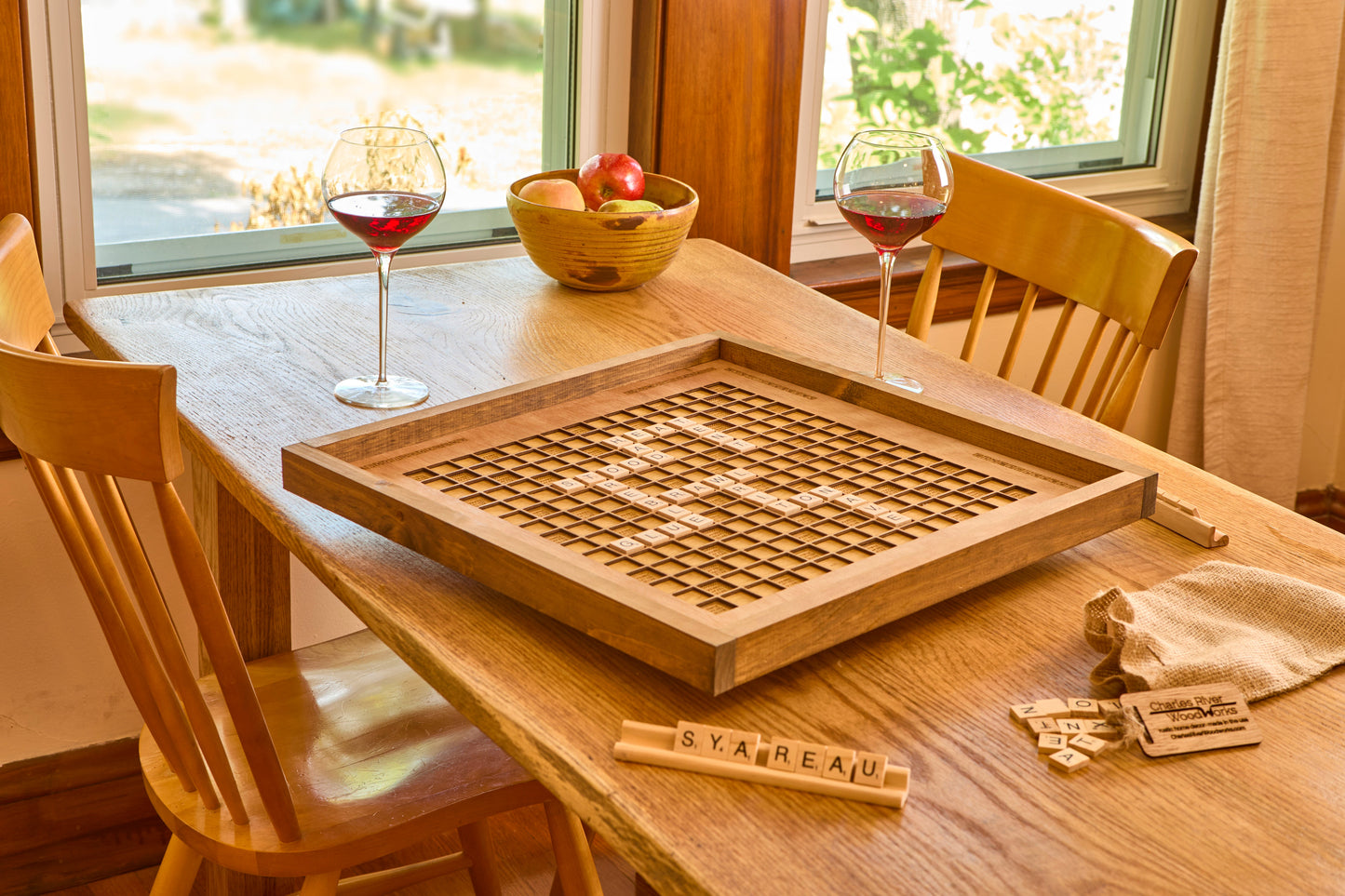 Wooden scrabble board on a table with chairs and a window in the background