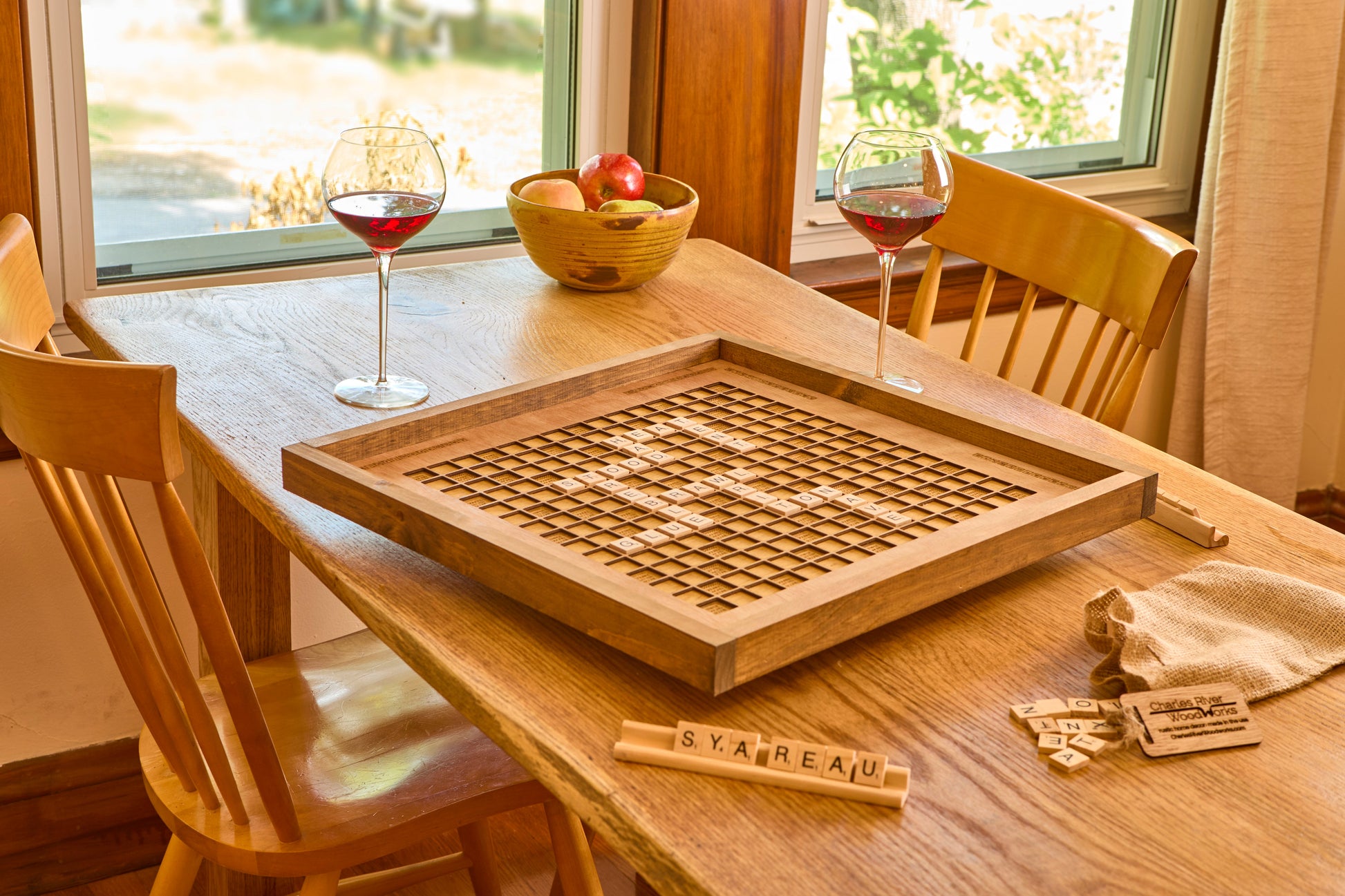 Wooden scrabble board on a table with chairs and a window in the background