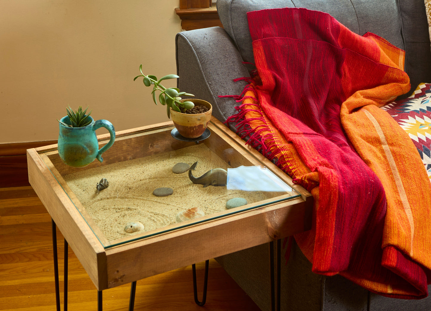 Wooden tray with decorative items on a table next to a sofa with colorful cushions.
