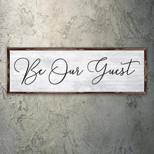 Decorative sign with 'Be Our Guest' text on a textured wall.