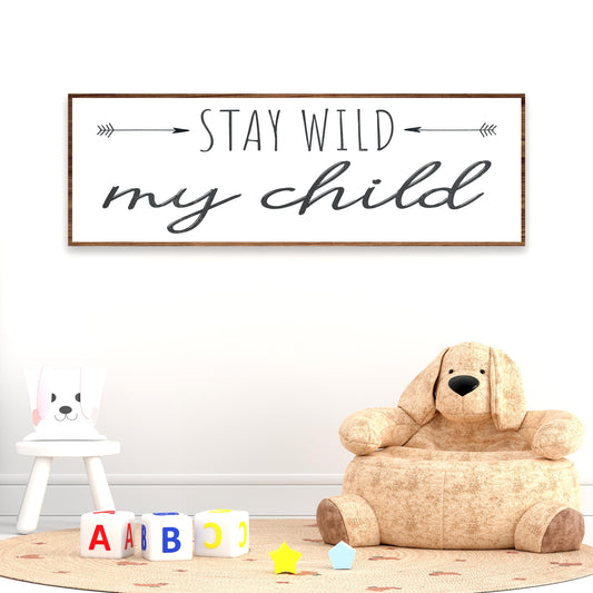 Wooden sign with 'Stay wild my child' text in a room with a teddy bear chair and alphabet blocks.