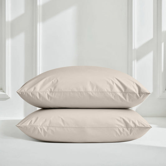 Two beige pillows on a light gray surface with a white paneled wall background