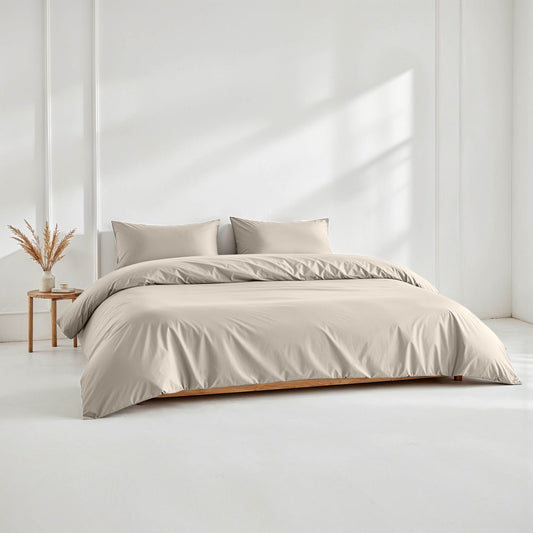 Beige bedding set on a bed in a minimalistic room with a side table and plant.