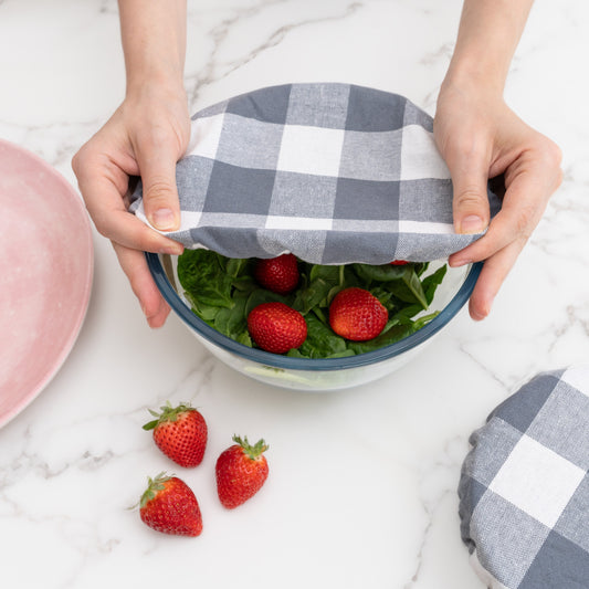 Person holding a bowl with a checkered cover, surrounded by strawberries on a marble surface. Checkered cloth covering a bow. Elastic for proper fit. Flax Linen.