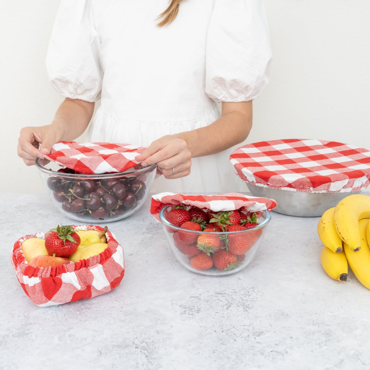 Person arranging fruits in glass bowls with red and white checkered covers on a light surface. Plaid cloth covering a bowl.  Elastic edge for proper fit. Flax Linen.