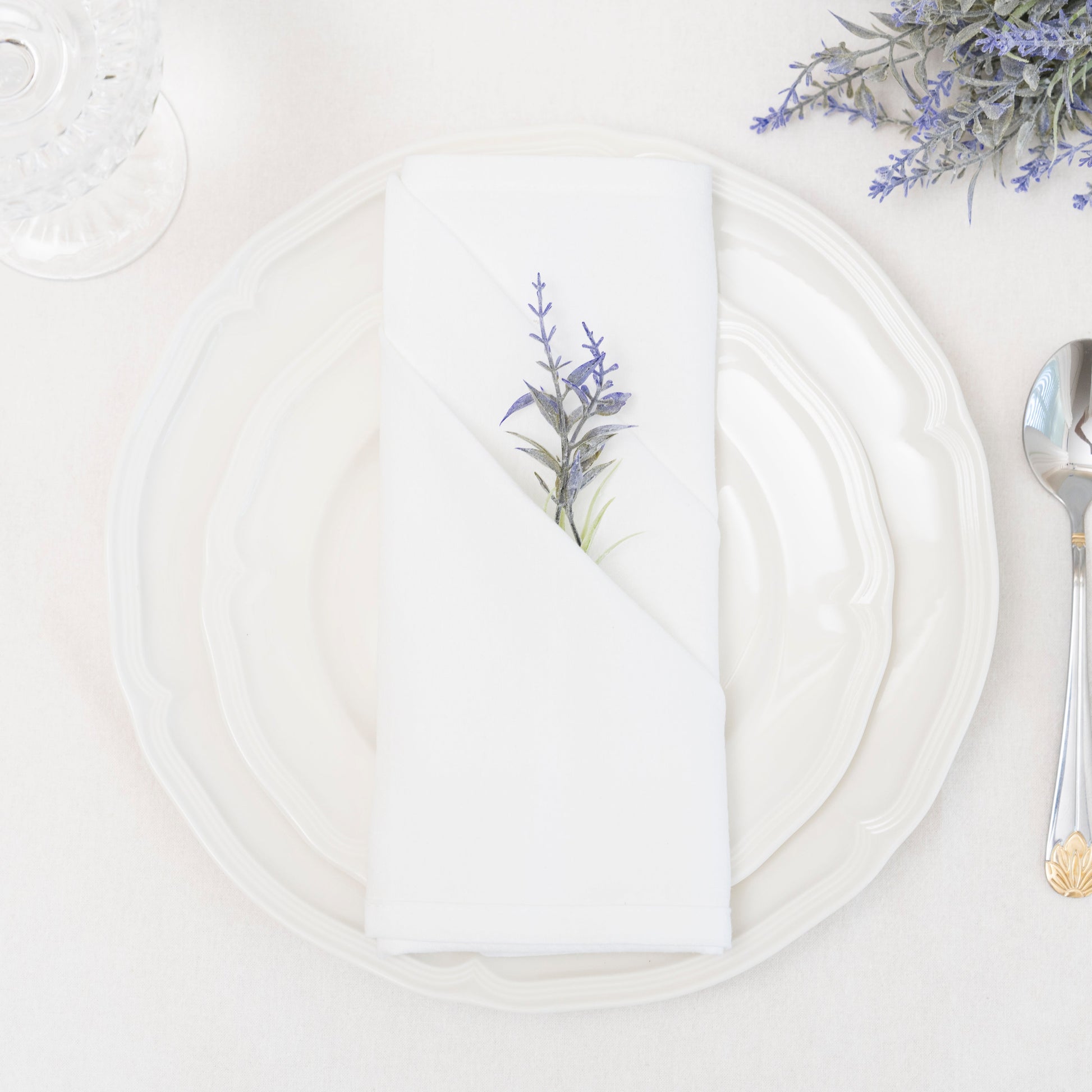 White plate with floral design on a white tablecloth, accompanied by a silver spoon.