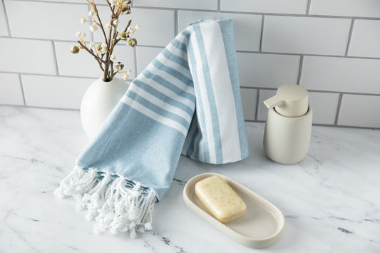 Blue and white striped towel with tassels on a marble surface with soap and a vase.